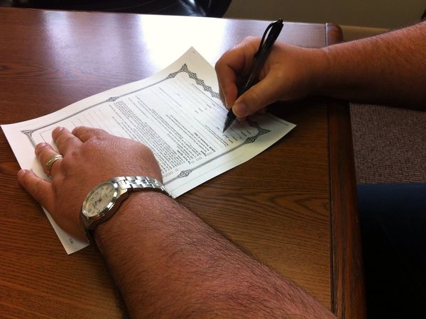 Hands filling out a printed form with a pen at a wooden table