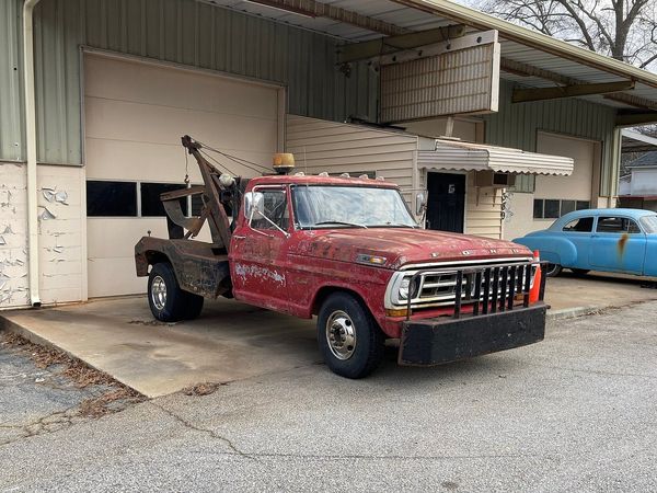 An older red tow truck with a rear towing boom parked outside a garage