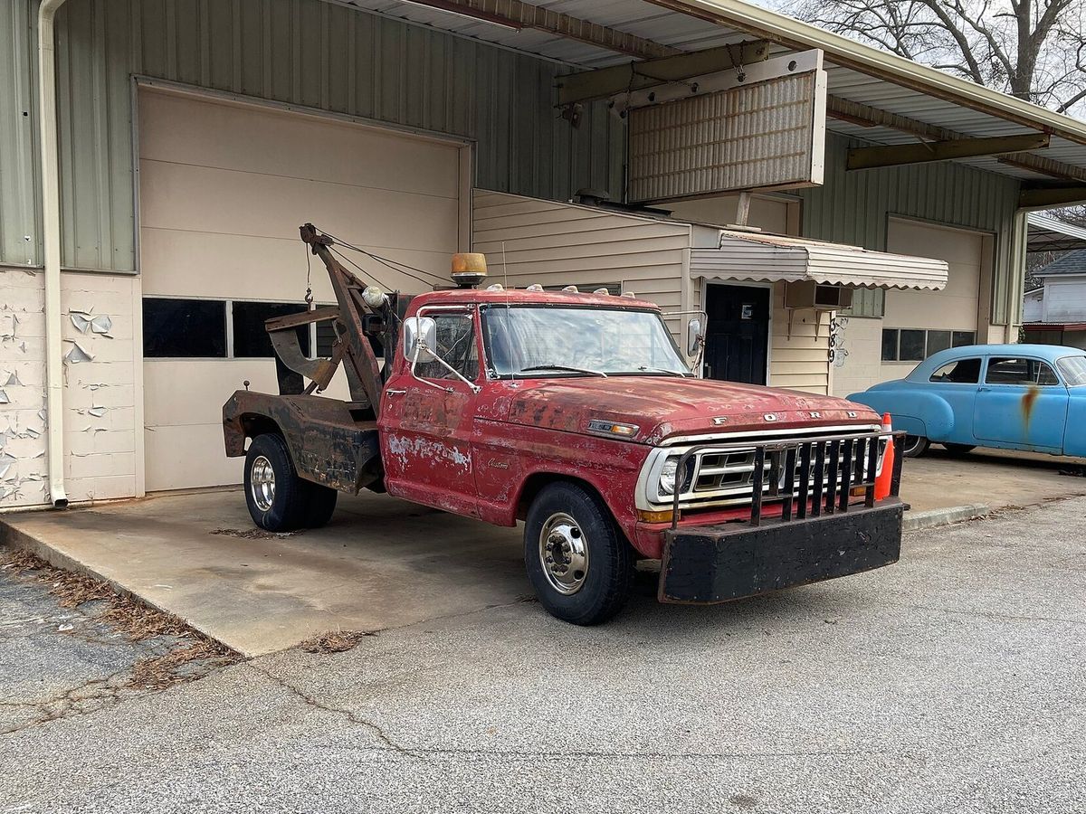An older red tow truck with a rear towing boom parked outside a garage